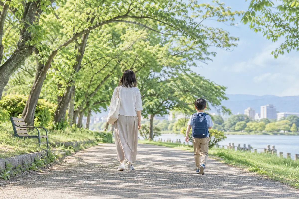 新緑の並木道を、少し離れて歩く大人と子どもの後ろ姿
