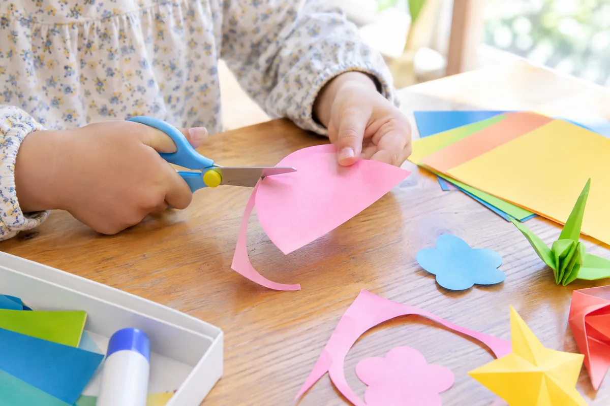 テーブルに広げた色紙を、はさみで切っている子どもの手元