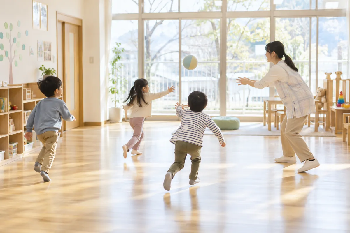 大きな窓のある部屋で、ボールを投げ合って走る子どもたち